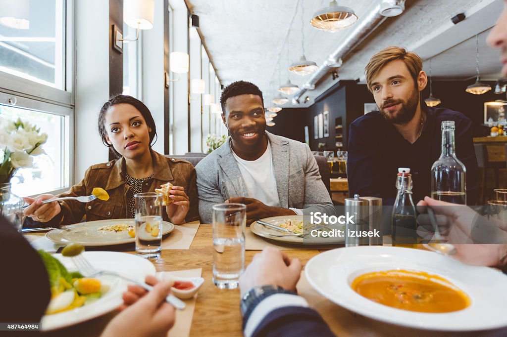 Multi ethnic group of friends eating dinner in a restaurant Multi ethnic group of friends - caucasian and afro american - eating dinner in the restaurant.  Friendship Stock Photo