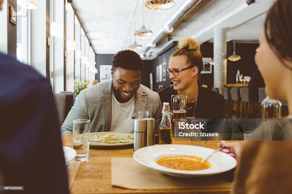 Multi ethnic group of friends eating dinner in a restaurant Multi ethnic group of happy friends - caucasian and afro american - eating dinner in the restaurant. Blonde woman wearing nerd glasses drinking beer. Restaurant Stock Photo