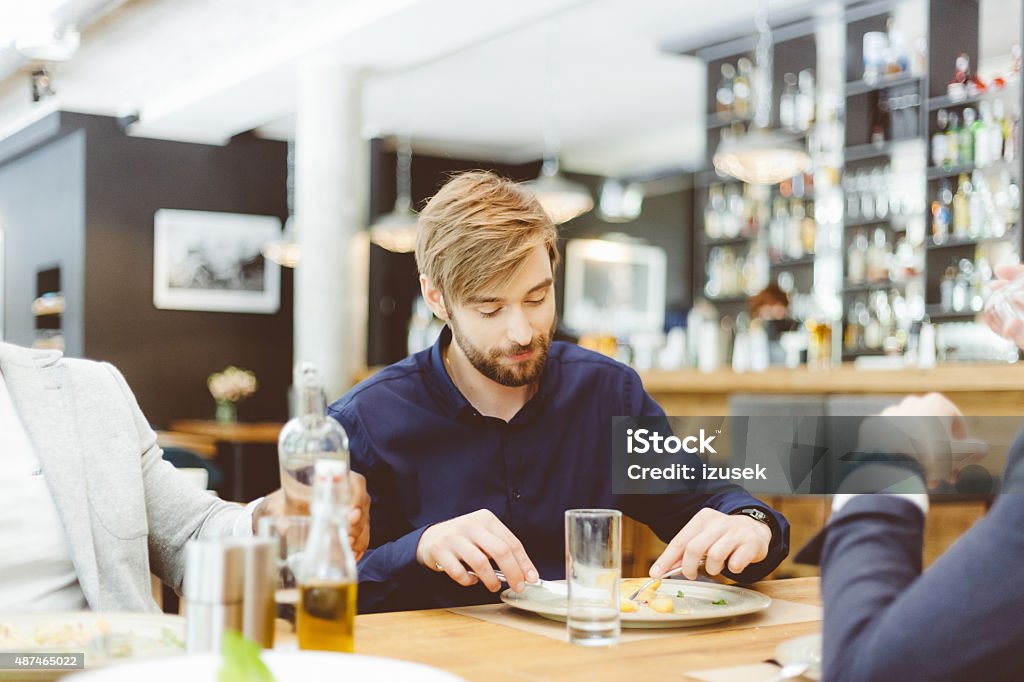 Friends eating dinner in a restaurant Three man eating lunch or dinner in the restaurant. Focus on bearded man.  2015 Stock Photo