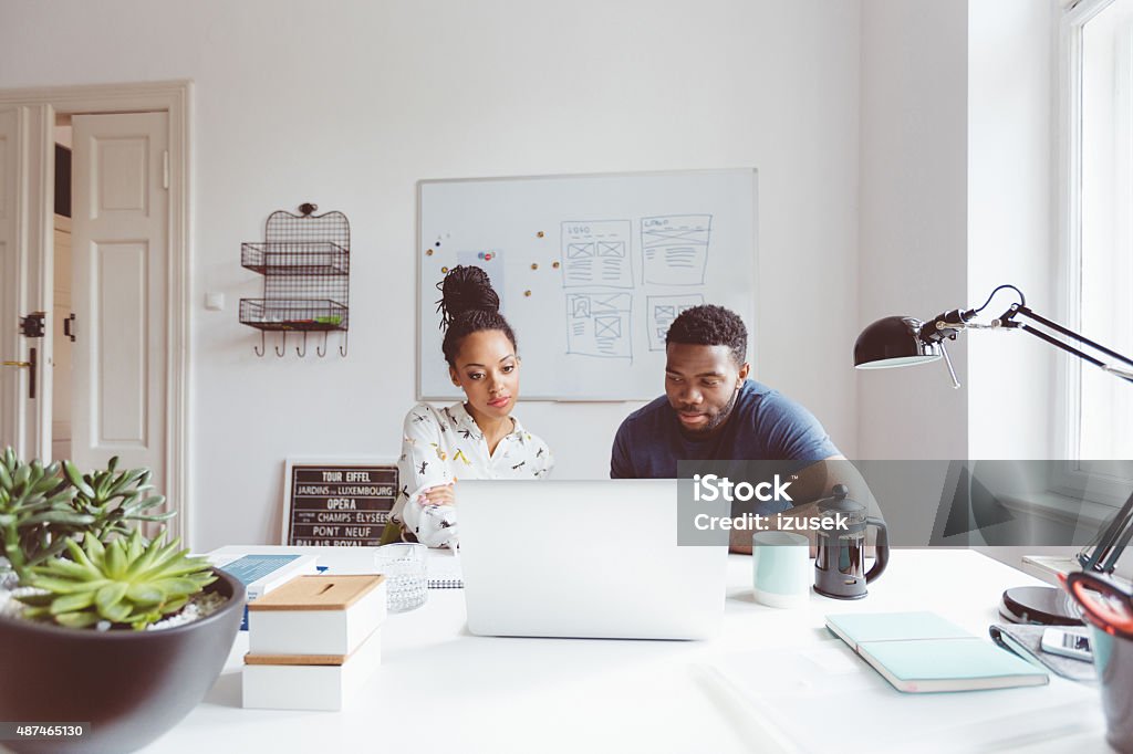 Start-up agency, afro american woman and man collaborating Afro american woman and man working together in the start-up agency, sitting at the table and using laptop.  2015 Stock Photo