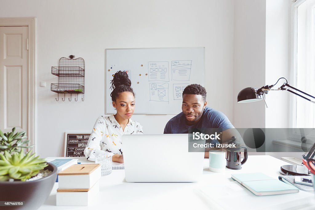 Start-up agency, afro american woman and man collaborating Afro american woman and man working together in the start-up agency, sitting at the table and using laptop.  Working At Home Stock Photo