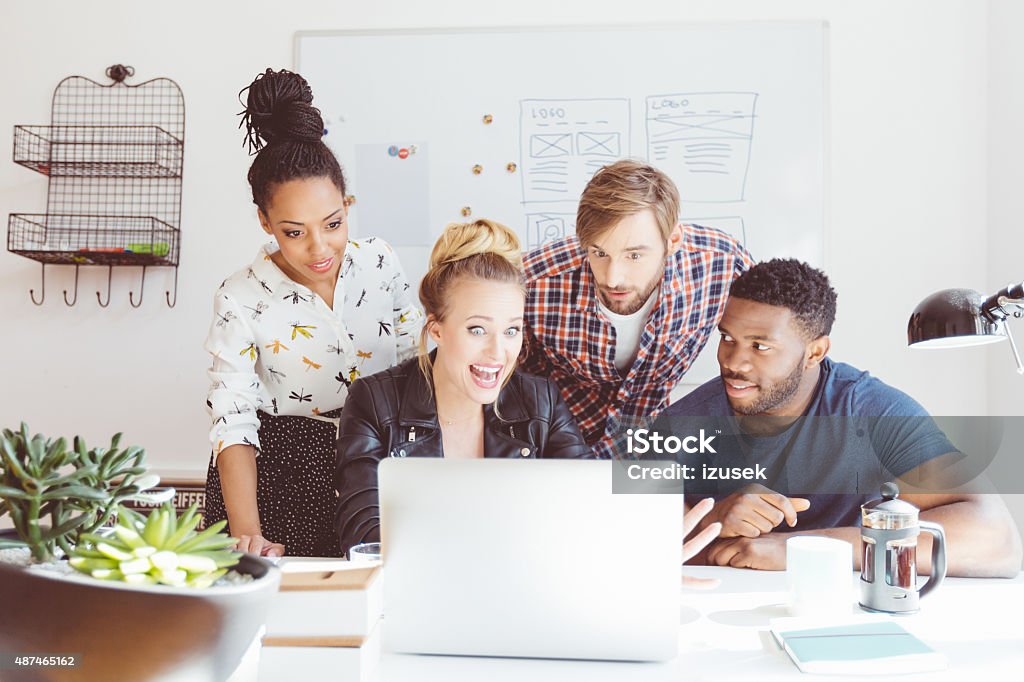 Start-up agency, excited multi ethnic group using laptop Start-up agency. Multi ethnic group of colleagues watching at computer screen with excited facial expression.  Ecstatic Stock Photo