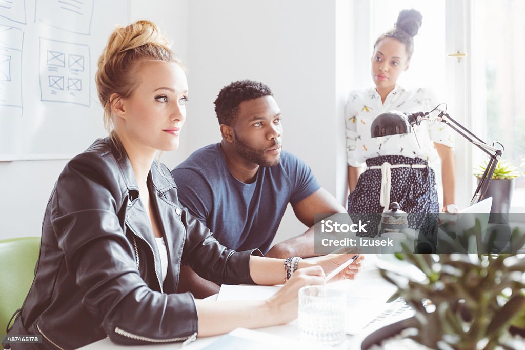 Start-up agency, multi ethnic group brainstorming Start-up agency. Multi ethnic team of designers - caucasian and afro american - meeting in an office.  2015 Stock Photo