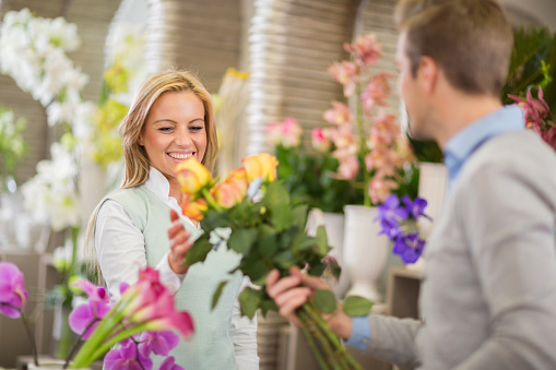 Happy mid adult woman buying bouquet of roses in a flower shop.