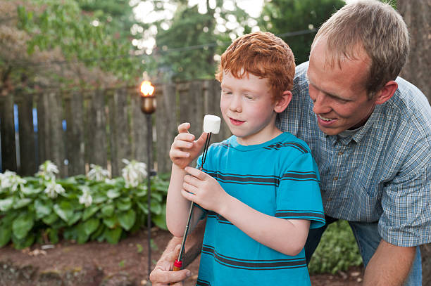 Father helping his boy prepare a marshmallow. stock photo