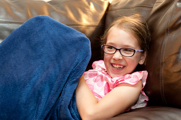 Niño de primaria girl snuggles en manta en el sillón. - foto de stock