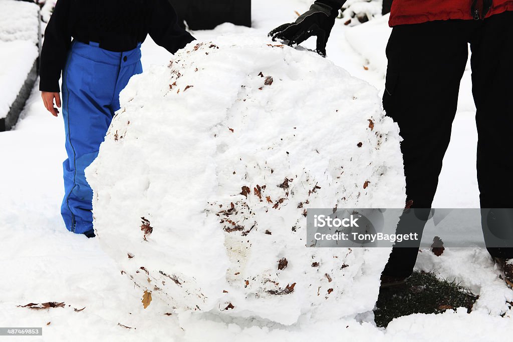 Rolling A Snowball Adult and child rolling a snowball to make a snowman after a heavy fall of snow in an urban park Adult Stock Photo