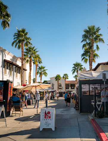 La Quinta, United States  - February 14, 2015: Vertical image taken in Old Town La Quinta during the Art UnderThe Umbrellas show and sale.  Vendors and customers can be seen in the image with the white, Old Spanish buildings of the downtown visible to the left of the image.  This show and sale happens several times during the winter tourist season and draws artists and artisans from around California and other southwestern states.  This image was taken during the day in early February.California