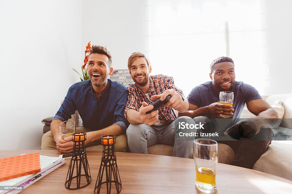 Three guys playing video games Multi ethnic - caucasian and afro american - friends sitting on sofa at home, playing video games and drinking beer.  Beer - Alcohol Stock Photo