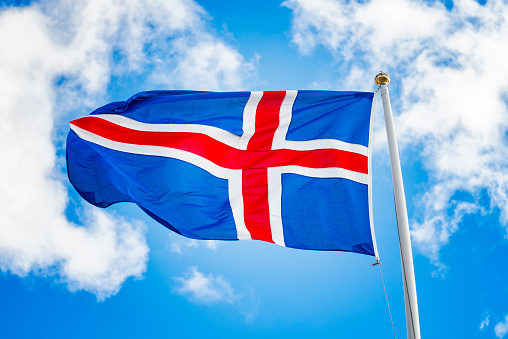 National flag of Iceland. Icelandic flag against blue sky and white clouds