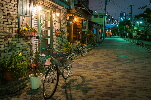 Bicycles standing on a quiet residential street beside a warmly lit cafe bar in the tranquil night air of central Tokyo, Japan. ProPhoto RGB profile for maximum color fidelity and gamut.