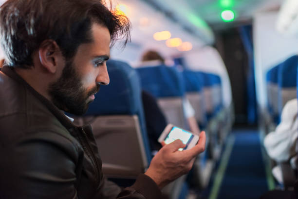 istock Young man text messaging on mobile phone in airplane. 487491284