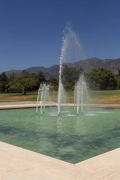 Blue spraying fountain of water with the mountains in the background at Los Angeles Arboretum gardens in California, United States, August 2015 – Editorial use only