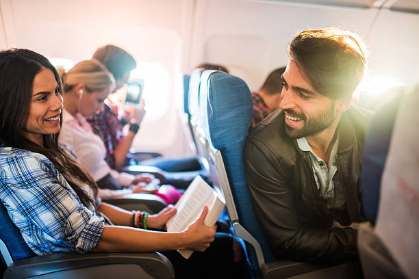 Young smiling man flirting with beautiful woman in airplane. Happy man communicating with young woman who is sitting behind him. They are traveling by airplane. economy class stock pictures, royalty-free photos & images