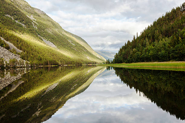 Beautiful  Norwegian landscape with  a lake.  Reflections from the nature  in the calm water just before sunset. Strong light illuminating the hillside. In background a view to Rondane mountain range and Rondane National Park.  Sel, Gudbrandsdalen, Norway
