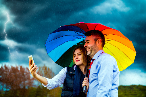young couple under umbrella making photo in rainy day.