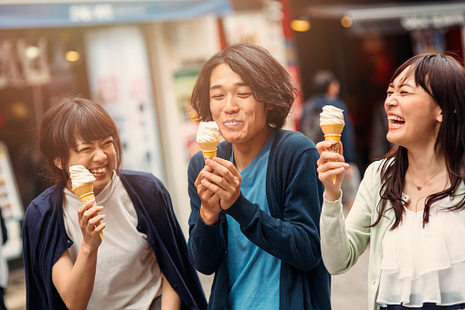 Happy japanese friends eating ice cream outside in the city.