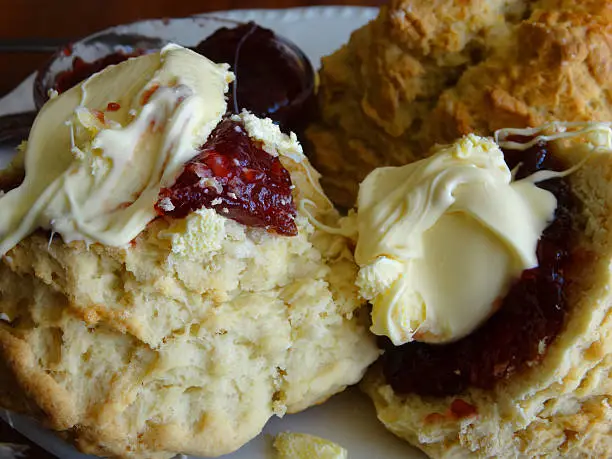 Photo showing a close-up of some homemade scones that have been served with strawberry jam and clotted cream, as part of an afternoon tea.