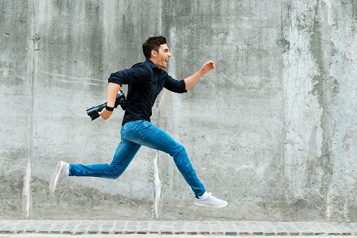 Full length of young photographer running against a concrete wall