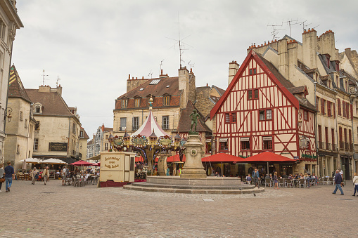 Dijon, France - August 16, 2015: Place du Bareuzai in Dijon, France. The François Rude Square (or Place du Bareuzai) is a square in the city center of Dijon, in the conservation area, subscribed since July 4, 2015 World Heritage UNESCO1. It bears the name of the sculptor François Rude. Many tourists walking on the square. A Carousel behing the statue.