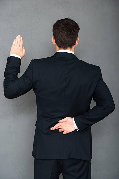 Telling lies. Rear view of young businessman keeping his fingers crossed and arm raised while standing against grey background hands behind back stock pictures, royalty-free photos & images