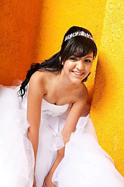 A 15 year old hispanic girl celebrates her birthday with a tiara and fancy white dress