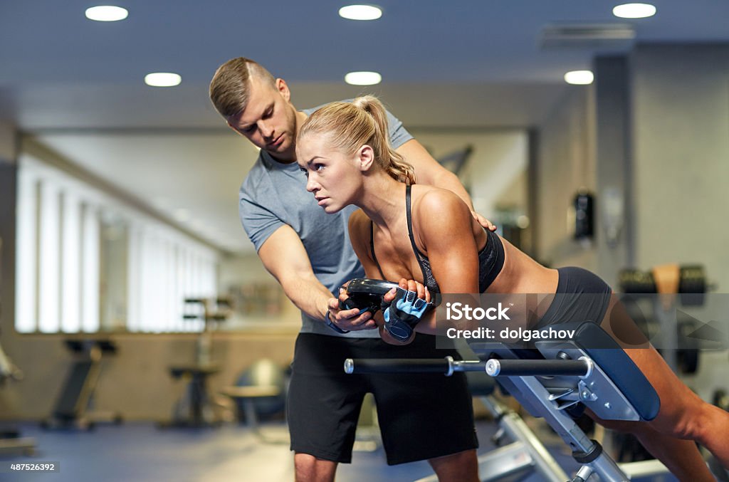 woman with personal trainer flexing muscles in gym sport, training, fitness, lifestyle and people concept - young woman with personal trainer flexing back and abdominal muscles on bench in gym 2015 Stock Photo