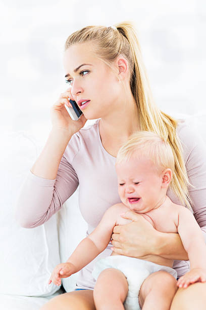 istock Woman holding crying baby talking on mobile phone 487527532