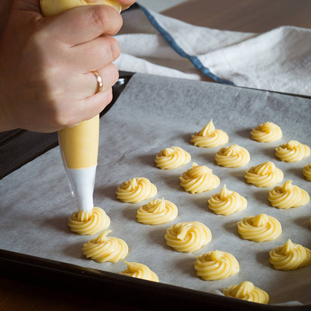 Unbaked cream puffs on parchment-lined baking sheet Piping choux paste for cream puffs onto parchment-lined baking sheet choux pastry photos stock pictures, royalty-free photos & images