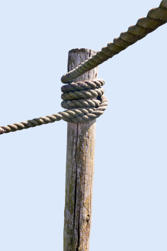 Wooden post with knotted rope leading in two directions. Isolated on light blue, copy space.