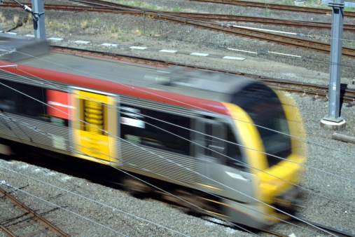 A blurred moving train in a rail yard in full sun.