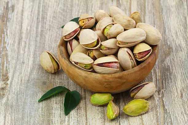 Pistachios with and without shell in wooden bowl with copy space