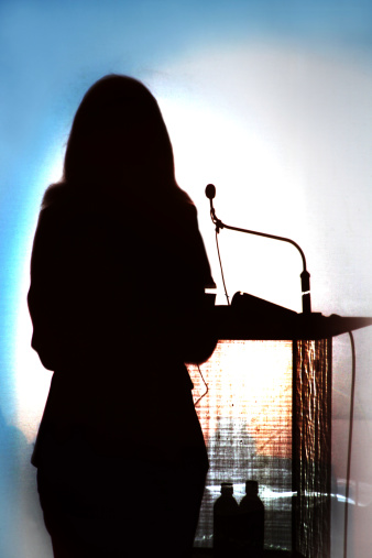 Shadow of speaker against a bright background at a congress. Silhouette of woman giving a presentation.