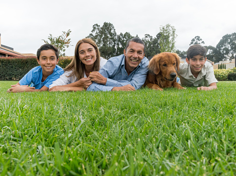 Latin family looking happy outdoors lying on the grass with a beautiful dog