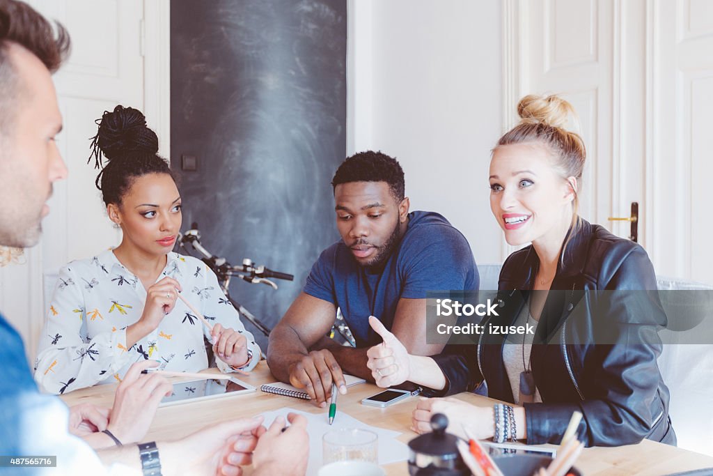 Start-up agency, multi ethnic team brainstorming Start-up agency. Multi ethnic team of designers - caucasian and afro american - meeting in an office, sitting at the table, discussing, brainstorming. 2015 Stock Photo