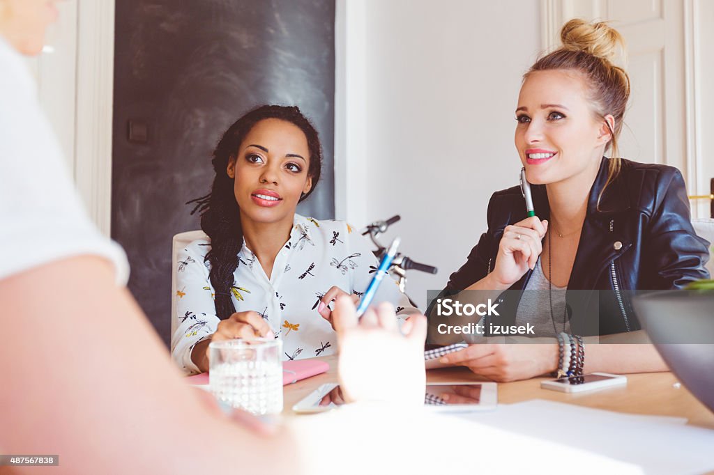 Women discussing in an office Start-up agency. Three women - caucasian and afro american - sitting at the table in an office and discussing. New Business Stock Photo