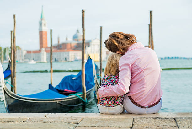 istock mother and daughter sitting together cuddling at water's edge 487584452