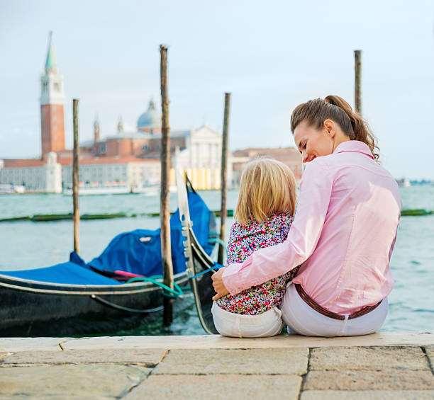 istock mother and daughter sitting near gondolas in venice 487584512