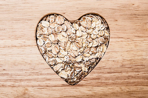 cereal de aveia em forma de coração na superfície de madeira. - oatmeal breakfast healthy eating cholesterol - fotografias e filmes do acervo