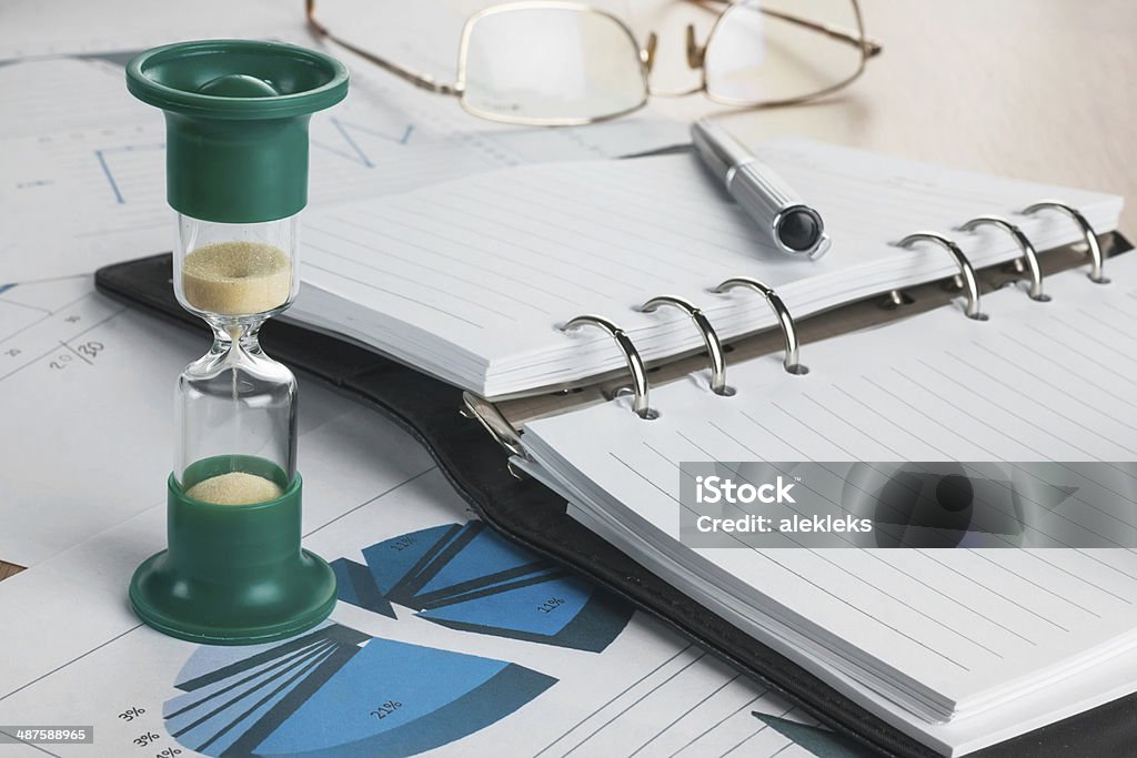 Hourglass, diary, glasses and pen Hourglass, diary, glasses and pen lying on a background of diagrams and graphs Backgrounds Stock Photo