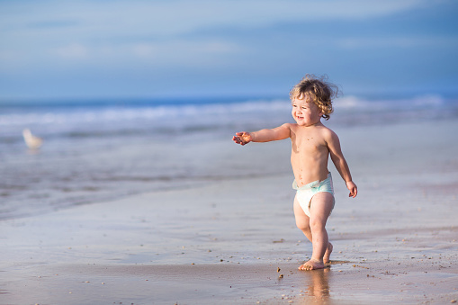 Funny little baby girl running on a beautiful tropical beach on a sunny warm summer evening