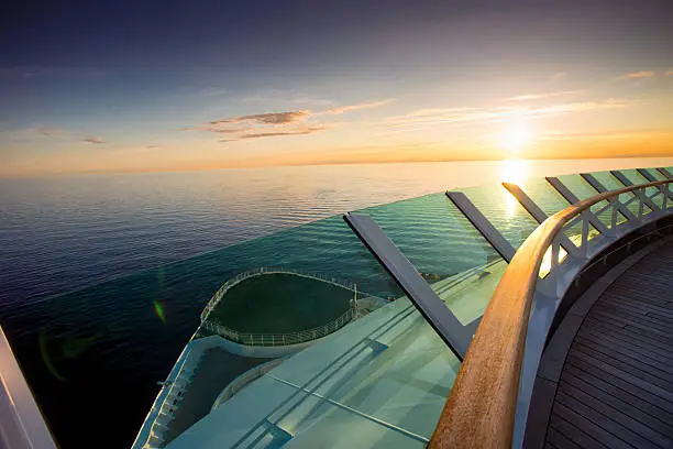 Beautiful sunset framed from the bow of a luxury cruise ship in a vast, calm ocean.