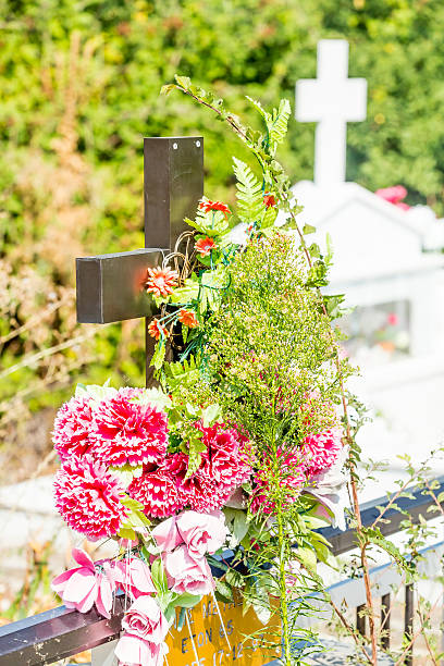 A white chrysanthemum bush in a ceramic flower pot is placed on a grey granite gravestone next to a cemetery candle. The simple memorial arrangement creates a peaceful atmosphere of remembrance and respect, symbolizing love and tribute to departed loved ones.