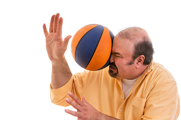 Man playing sport being hit by a basket ball Middle-aged balding man with a goatee playing sport being hit by a basket ball with force in the face when he misses a catch or as an unexpected accident to a spectator, on white eye catching stock pictures, royalty-free photos & images
