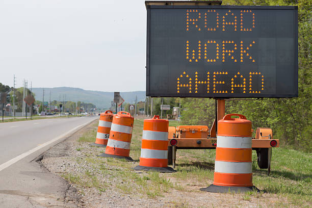 Road Work Ahead The road cones and lit sign indicate road work ahead.  No identifiable commerical signs, cars are in a distance out of focus. Copy space to left of sign. hazard sign photos stock pictures, royalty-free photos & images