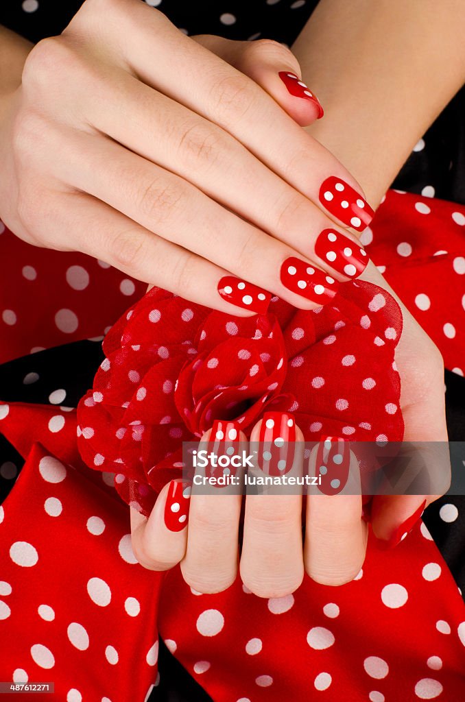 Beautiful female hands with red manicure and white dots. Close up on beautiful female hands. Black and red dotted background. Manicure Stock Photo
