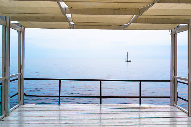 Minimalistic symbolic composition with anchor railing in focus and blurred yacht on calm sea, representing solitude, reflection, and freedom.