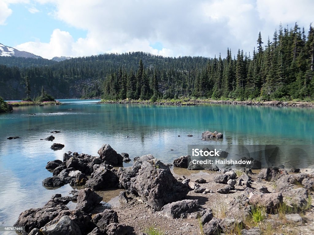 Turquoise Lake, rocks, and forest Rocky shore in foreground, turquoise colored lake in center, with forests and mountains in the background. Autumn Stock Photo