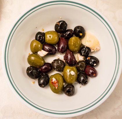 Black and green olives sit side by side on a small dish with small pieces of white cheese and olive oil mixed in  with them.