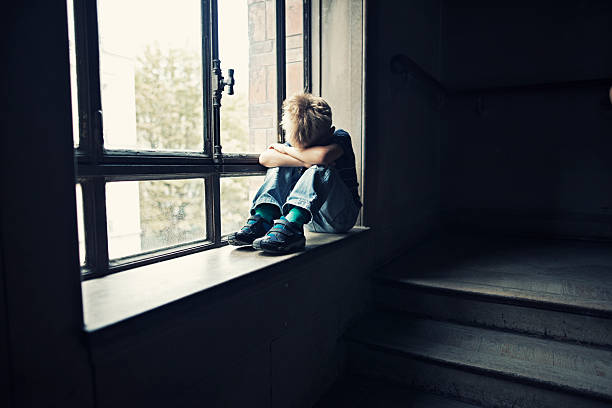 Depressed little boy in old staircase Depressed 6 years old child sitting on window in old staircase. The boy is crying hiding his head in arms.  child abuse photos stock pictures, royalty-free photos & images